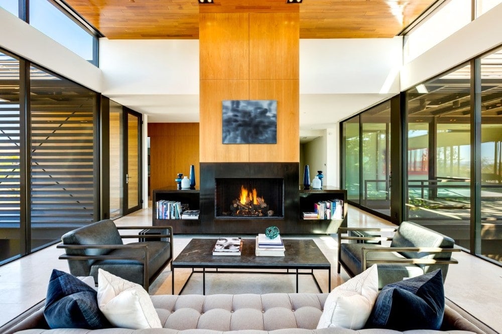 This closer look at the spacious and bright living room showcases the tall wood-paneled pillar that houses the fireplace across from the beige sofa that is paired with a couple of black leather armchairs. Image courtesy of Toptenrealestatedeals.com.