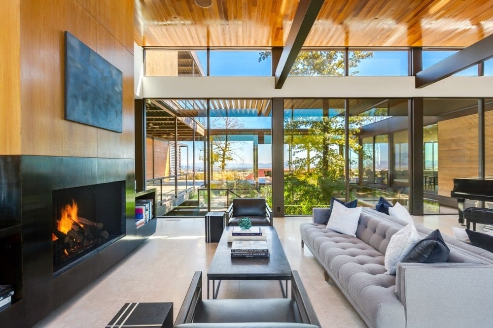 This is a closer look at the living room showcasing the dark coffee table that matches the dark mantle of the fireplace. On the far side you can see the large glass wall adorned with landscaping. Image courtesy of Toptenrealestatedeals.com.