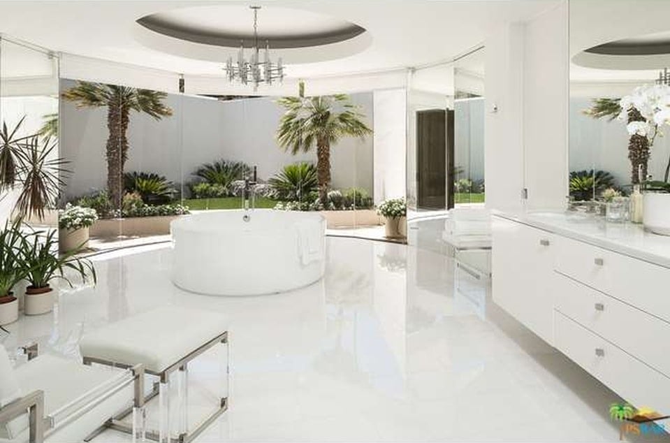 The bright white floor, walls, ceiling and freestanding bathtub of this bathroom are complemented by the green landscaping just outside the glass walls on the far side. Image courtesy of Toptenrealestatedeals.com.
