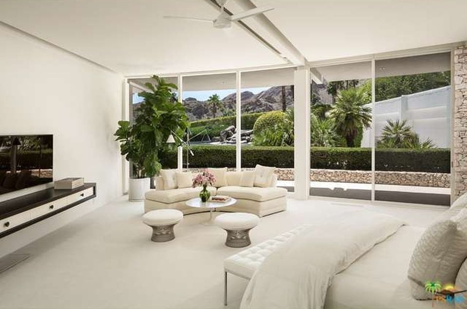 This is a bright and airy spacious bedroom with a beige bed, beige walls and ceiling. These are then complemented by the potted plant at the far corner that matches the landscape outside the glass wall. Image courtesy of Toptenrealestatedeals.com.