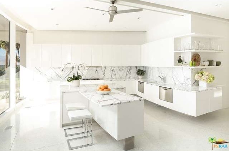 This other look at the kitchen showcases the T-shape of the kitchen island that also has a countertop extension for the breakfast bar paired with a couple of modern white stools. Image courtesy of Toptenrealestatedeals.com.