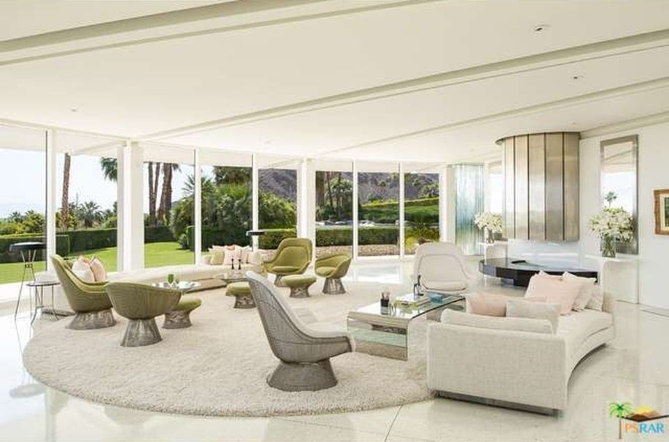 This is a look at the large open area of the living room illuminated by the curved wall of glass and warmed by the fireplace. Image courtesy of Toptenrealestatedeals.com.