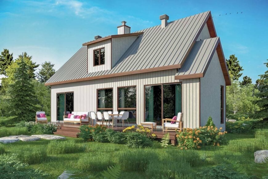 Angled rear view with dormer window, sliding glass doors, and an open deck filled with white cushioned chairs and a rectangular dining set.