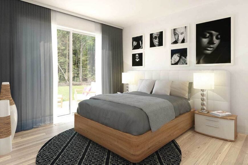 The primary bedroom has wooden furnishings, contemporary decors, a gallery wall, and a round area rug that lays on the light hardwood floor.