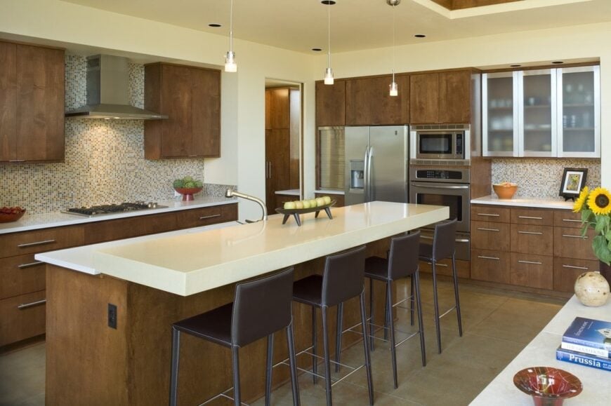 Kitchen with wooden cabinetry, stainless steel appliances, and a two-tier breakfast island lines with brown counter chairs.