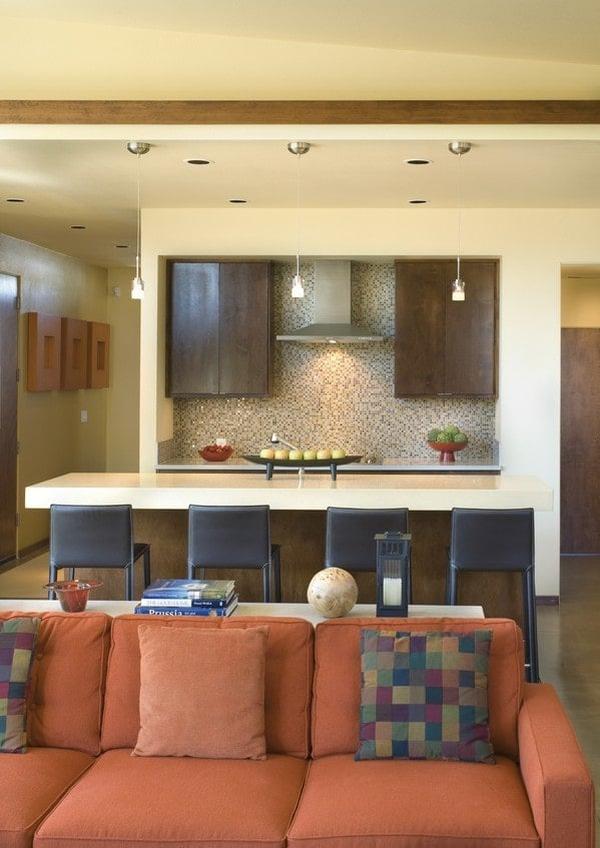 Sitting across the breakfast island is the built-in cooktop and sleek vent hood fixed against the mosaic tile backsplash.