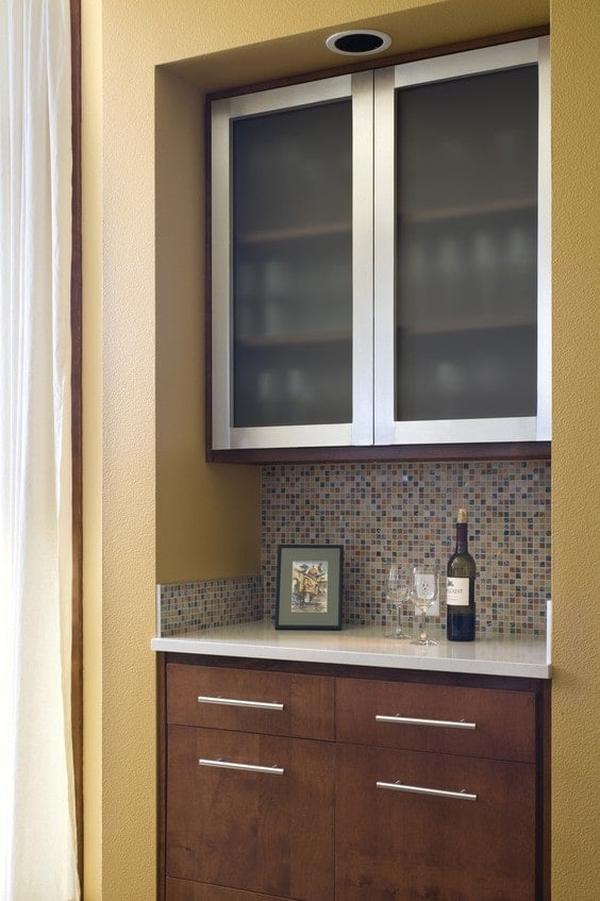 Small bar with wooden drawers and a glass front upper cabinet.