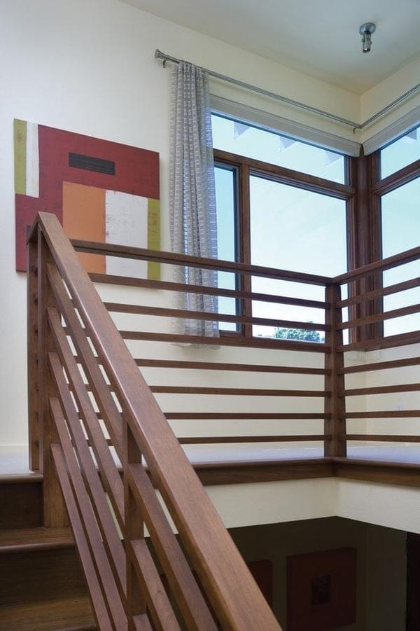 Second-floor balcony with wooden railings and white walls adorned with multi-colored artwork.