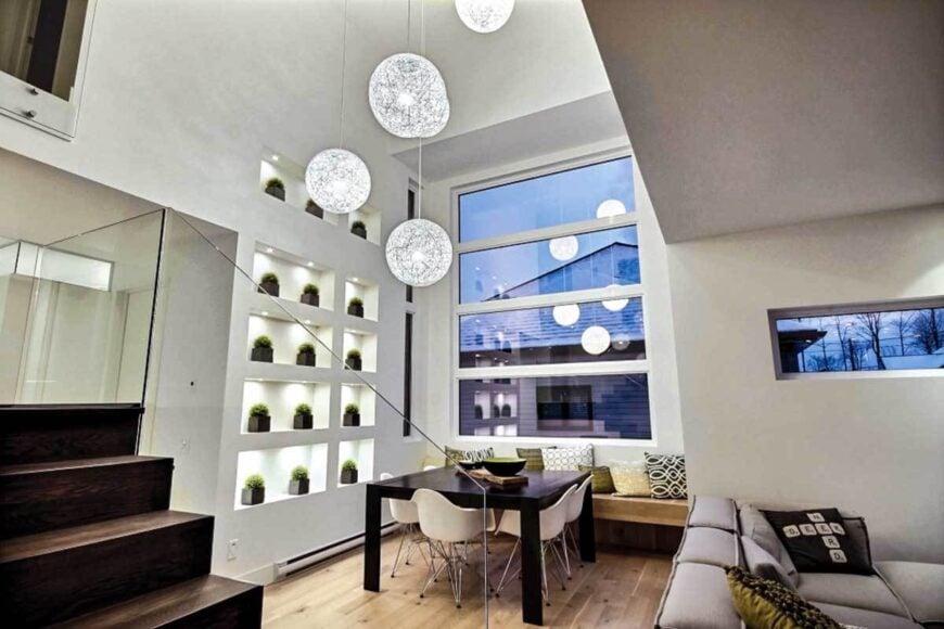 The dining area offers a dark wood dining table, white modern chairs, and a built-in bench filled with patterned pillows.