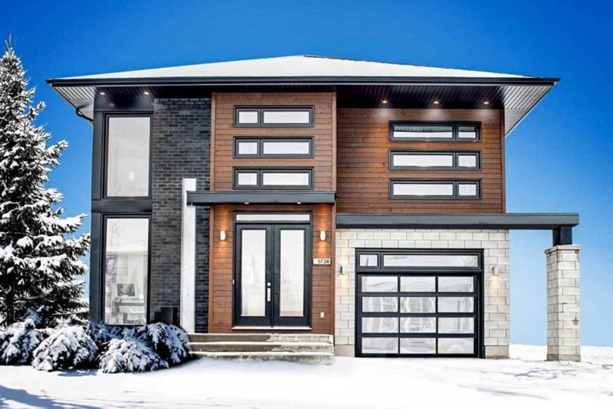 Front view of the house during winter showcasing its sleek and clean architectural design accentuated with stone brick and wood-paneled exterior.