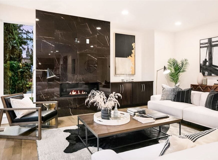 Living room with a marble fireplace, cozy cushioned seats, and a wooden top coffee table sitting on layered rugs.