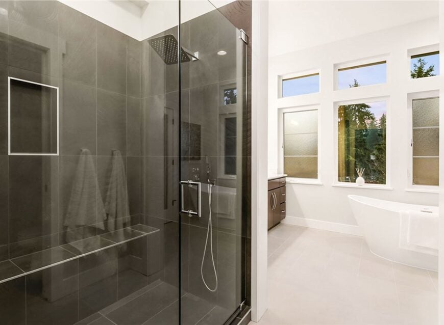 The walk-in shower showcases an inset shelf, chrome fixtures, and a tiled bench.