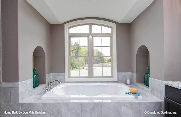 Arched inset wall niches filled with transparent green bottles flanked the drop-in bathtub.