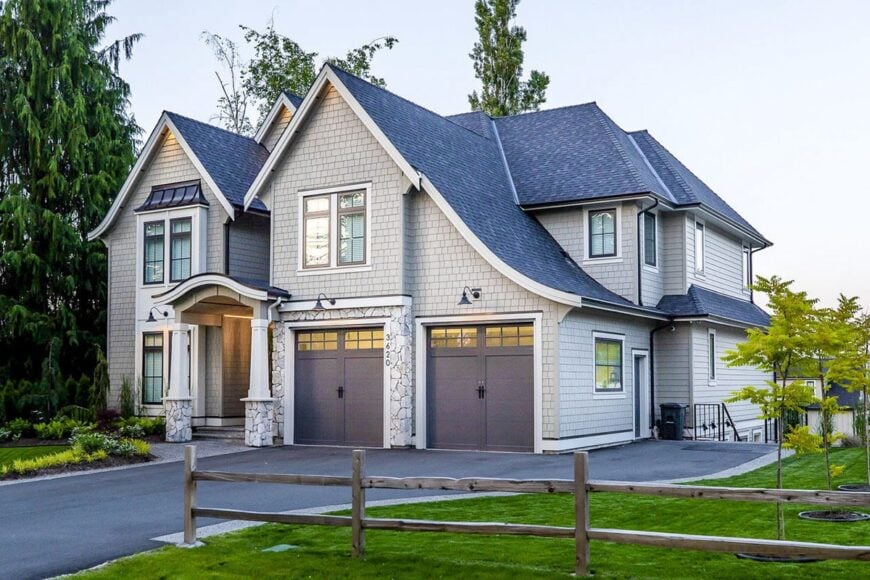 The home's angled front view showing the cedar shake siding, stone accents, and an arched front porch supported by tapered columns.