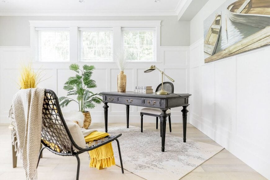 Study with cushioned and perforated chairs, dark wood desk, and a boat painting adorning the wainscoted walls.