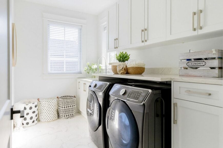 Utility with white cabinets, granite countertops, black front-load appliances, and patterned laundry bins.