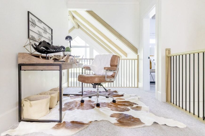 Second-floor loft that doubles as an office showcasing a wooden desk and leather swivel chair over a cowhide rug.