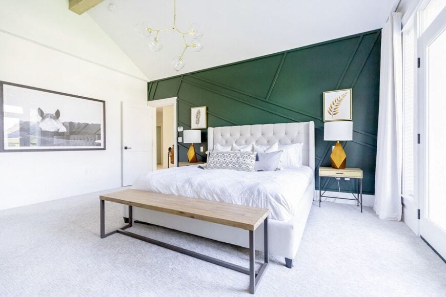 Primary bedroom with a striking green accent wall, carpet flooring, and a vaulted ceiling mounted with a contemporary chandelier.