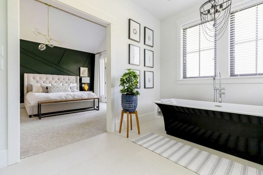 The primary bathroom features a freestanding tub complemented with a flower pedestal, striped runner, and an industrial chandelier.