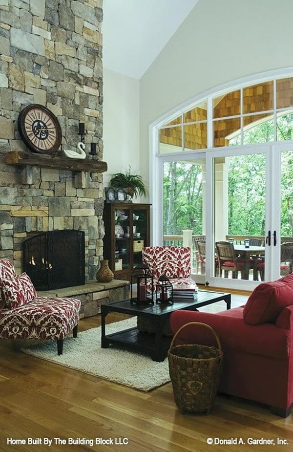 Living room with a red sofa, patterned chairs, a stone fireplace, and a dark wood coffee table sitting on a beige shaggy rug.