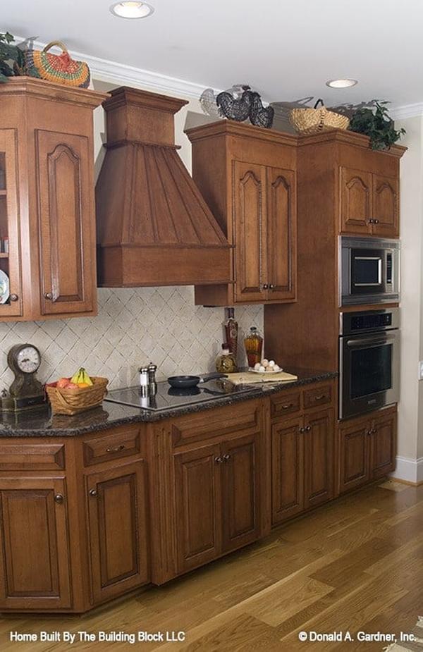 The kitchen is equipped with wooden cabinetry, stainless steel appliances, and a built-in cooktop fixed under the bespoke vent hood.