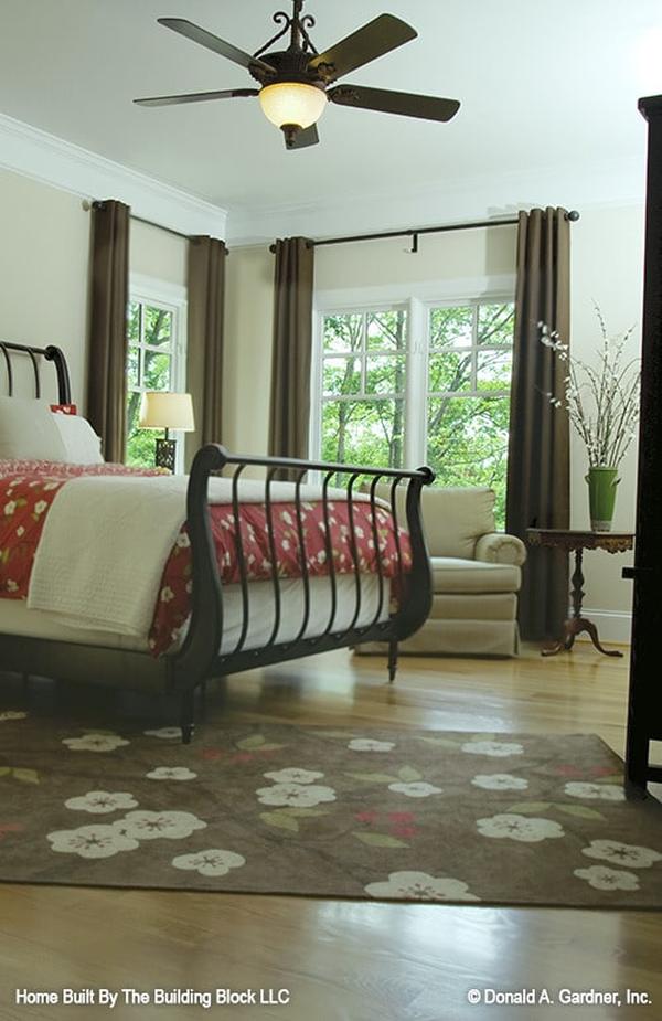 The primary bedroom offers a stylish metal bed, a skirted armchair, and a brown floral rug that lays on the hardwood flooring.