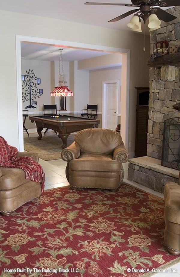 Recreation room with a billiards table, a stone fireplace, brown leather armchairs, and a red floral rug.