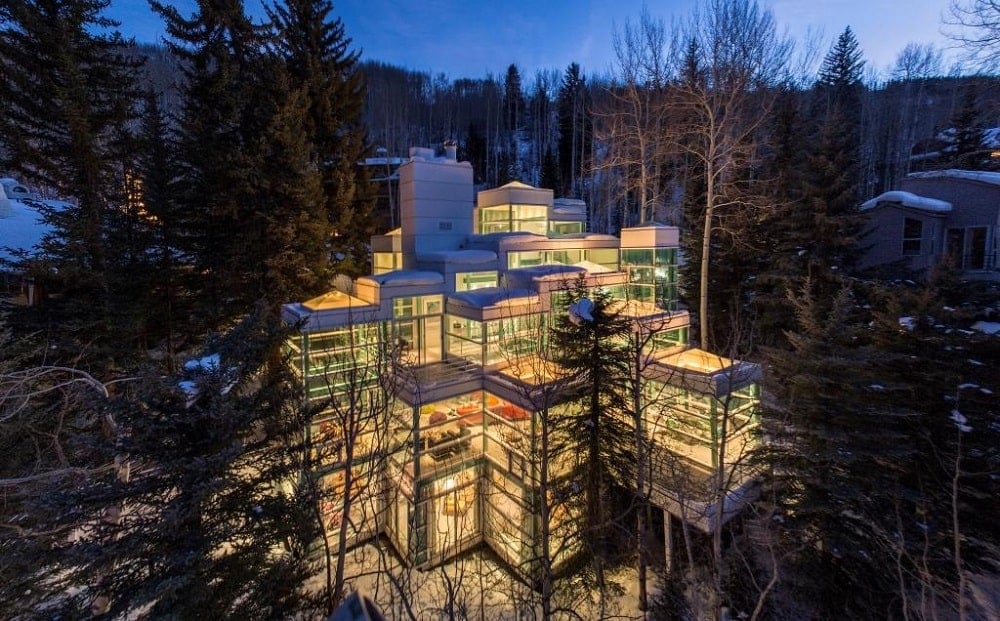 An aerial view of the house featuring the glass walls the make the house glow warm from the interior lights.