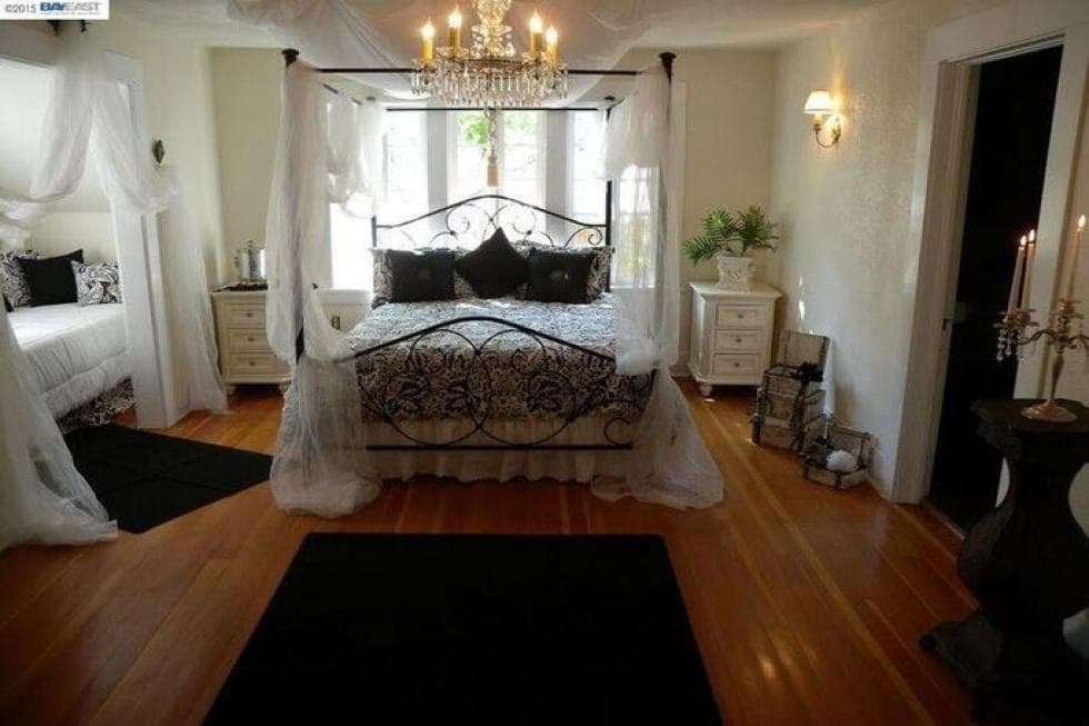 This bedroom has a wrought-iron four-poster bed with curtains that go well with the light tone of the walls complemented by the hardwood flooring. Image courtesy of Toptenrealestatedeals.com.