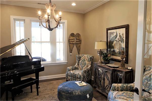The study has classy wingback chairs, round ottoman, baby grand piano, and a rustic console table adorned by a framed artwork.