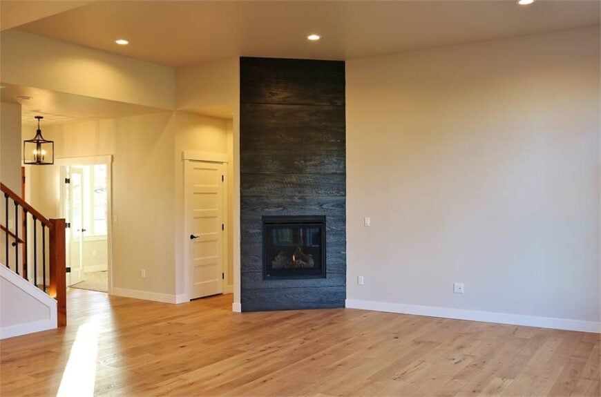 Living room with light hardwood floor, glass-enclosed fireplace, and beige walls.