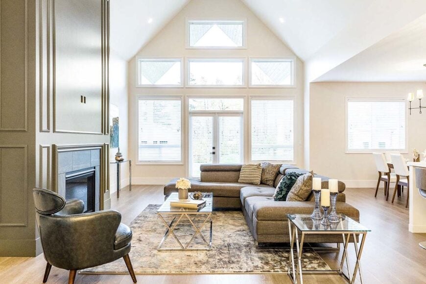 Living room with cathedral ceiling, glass-enclosed fireplace, an L-shaped sofa, round back chair, glass top tables, and a clerestory windows that invite natural light in.