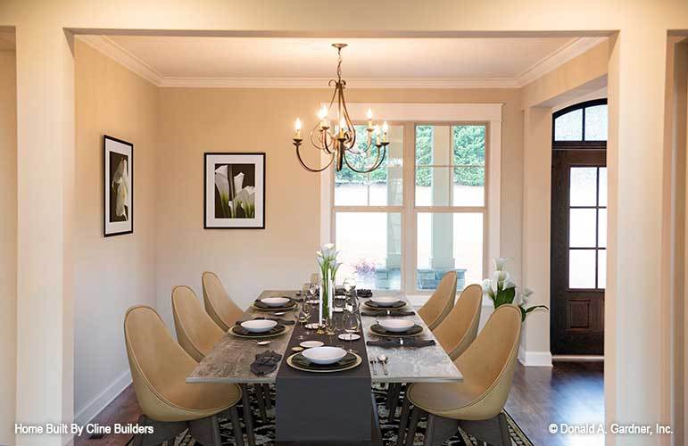 Formal dining room with a candle chandelier, round back chairs, rustic dining table, and black-framed artworks adorning the beige walls.