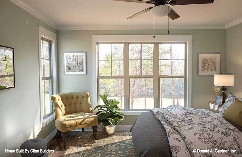 This bedroom has a cozy bed, tufted chair, fresh potted plant, and white framed windows inviting natural light in.