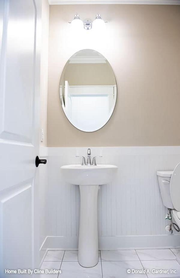 Powder room with a porcelain pedestal sink and an oval frameless mirror.