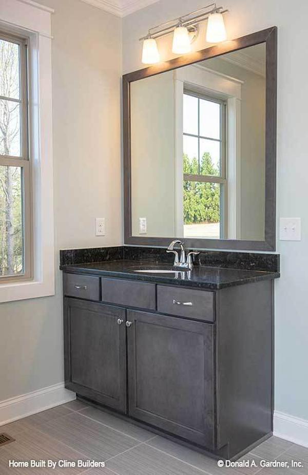 Another bathroom with dark wood vanity and a large framed mirror well-lit by glass sconces.
