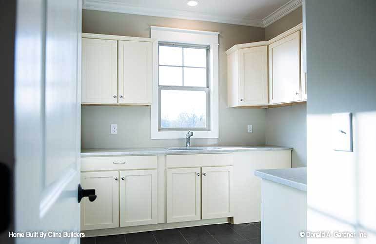 The utility room is filled with cream cabinets, undermount sink, and a white framed window.