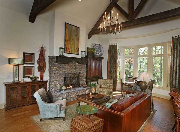 Living room with leather sofa, fabric armchairs, a stone fireplace, and a bow window dressed in patterned drapes.