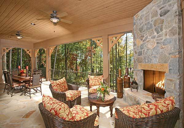 Covered lanai filled with a rectangular dining set, cushioned wicker chairs, and a large stone fireplace fixed in the corner wall.
