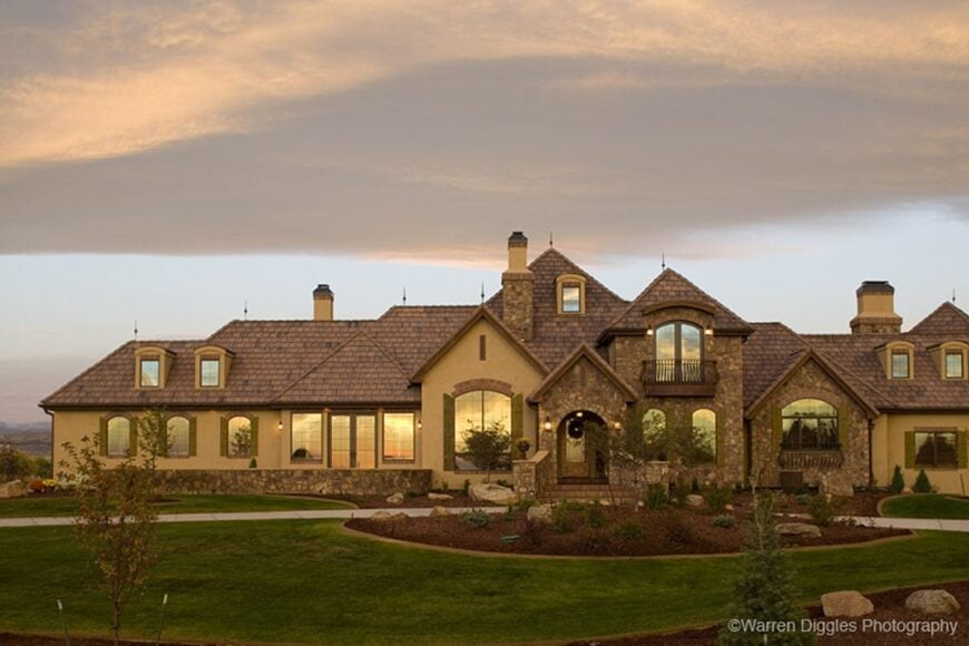 Front exterior view with hipped and gables, stone and stucco, and a covered entry framed with an archway.