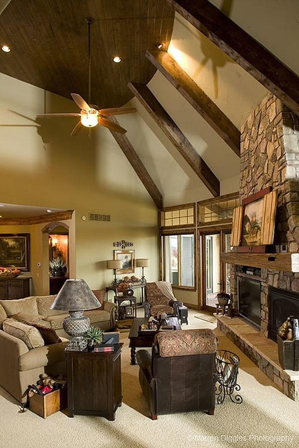 Living room with beamed ceiling, stone fireplace, beige sectional, and brown armchairs.