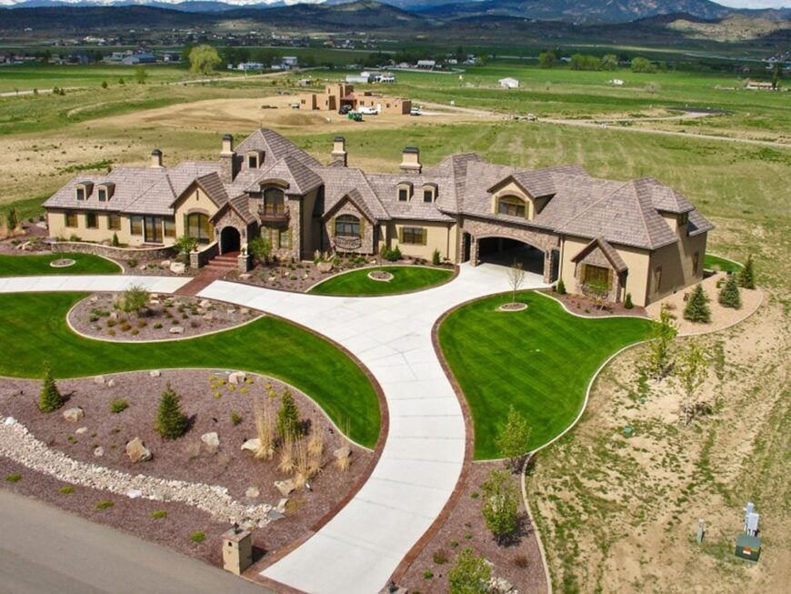 Aerial view showing wide French country home surrounded by the expansive green lawn.