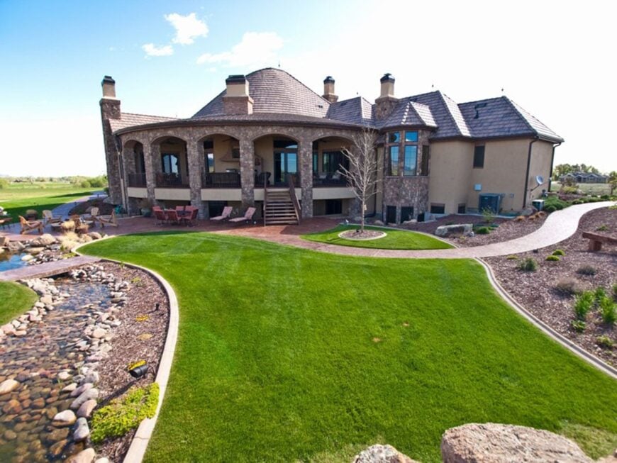Rear exterior view with covered deck, well-maintained lawn, and a man-made stream.