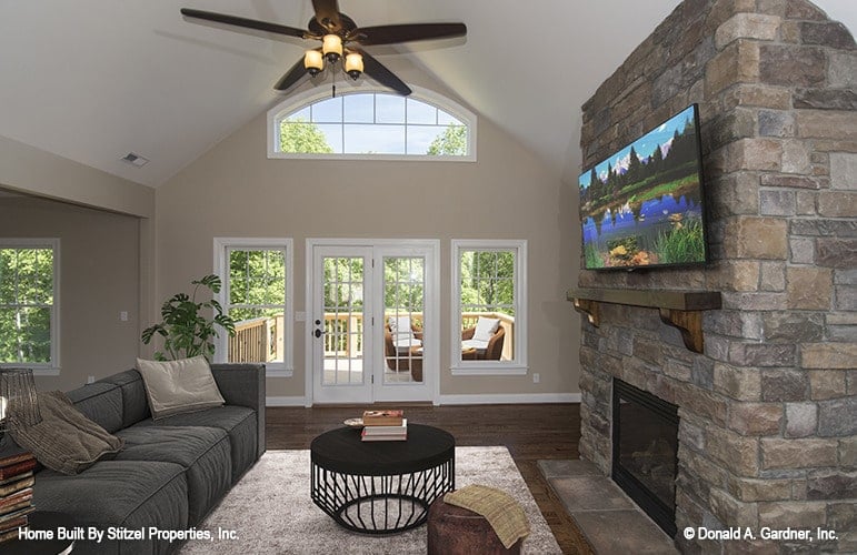 The living room has a cathedral ceiling, stone fireplace, gray sectional, and a glass door that opens to the deck.