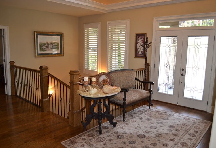 The foyer has a french entry door, an upholstered bench, round side table, and a floral area rug.