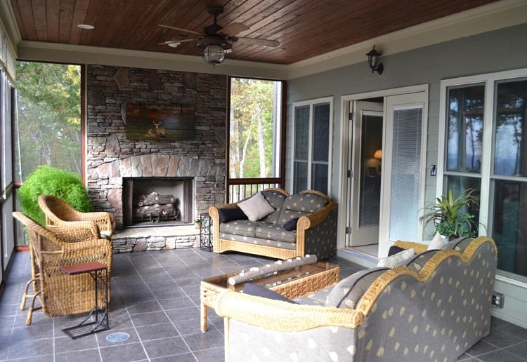 Screened porch with a stone fireplace, patterned sofas, wicker armchairs, and a matching coffee table.