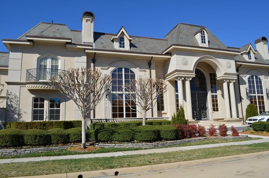 Home facade with tall arched windows, greek columns, intricate entry door, and hipped roofs adorned with dormers.