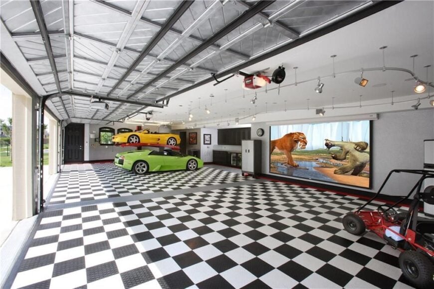 The oversized garage has a metal beamed ceiling, a checkered floor, black cabinets, and a large screen.