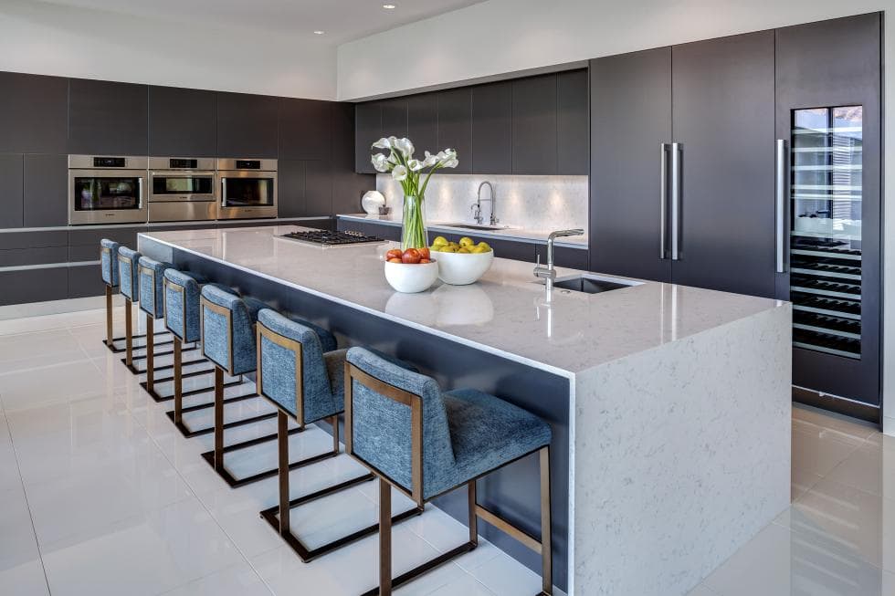 This kitchen has a large white waterfalls kitchen island that stands out against the gray modern cabinetry with stainless steel appliances. Image courtesy of Toptenrealestatedeals.com.
