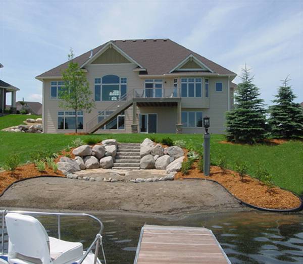 Rear exterior view showing the upper balcony, covered patio, and a stone staircase leading down the lake.